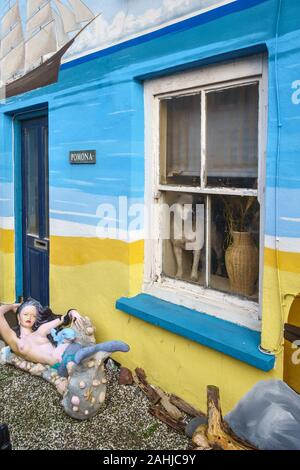 Borth, ein Küstendorf in der Nähe von Aberystwyth, Wales, Großbritannien. Ein Hund schaut aus dem Fenster eines hell bemalten Häuschens, mit einer Meerjungfrau im Vorgarten Stockfoto
