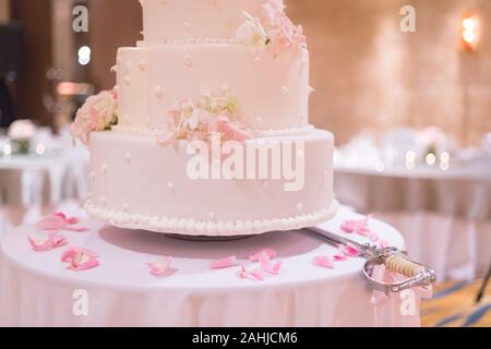 Hochzeit Schwert für Kuchen in der Nähe von Hochzeitstorte in zarten rosa Ton Dekorieren mit Blumen und einige Blütenblatt setzen Stockfoto