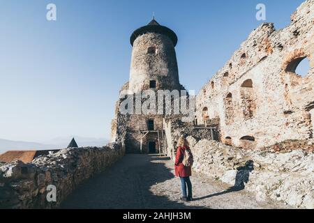 Frau im roten Mantel entdecken Lubovniansky Hrad Burgruinen in Stara Lubovna, Slowakei. Stockfoto