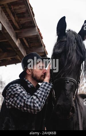 Porträt von einem Kerl in einem Hut mit einem schwarzen Pferd. Stockfoto