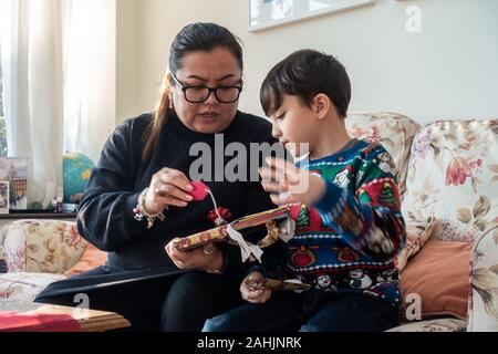 Eine Mutter und jungen Sohn aufgeregt ein Weihnachtsgeschenk gemeinsam öffnen Stockfoto