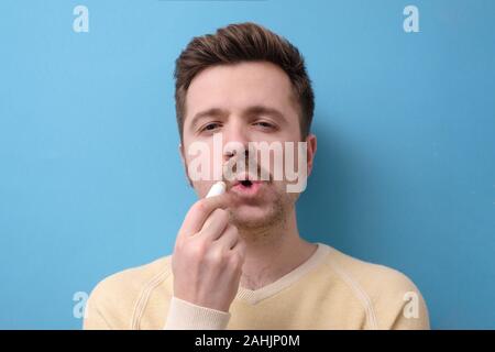 Guy Anwendung Balsam auf Risse trockene Lippen mit hygienischen Balsam auf blauem Hintergrund isoliert Stockfoto