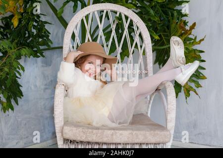 Porträt einer wunderschönen Modische kleine Mädchen mit Hut in einem Stuhl sitzend Stockfoto