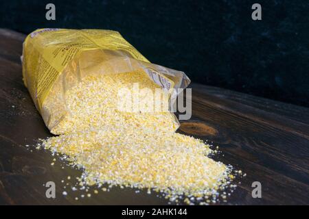 Grobe gelbe Maismehl gegossen auf ein Holz Tabelle: Grob Gemahlen gelber Maismehl verschütten aus der Tasche auf einem dunklen Holz Tisch Stockfoto