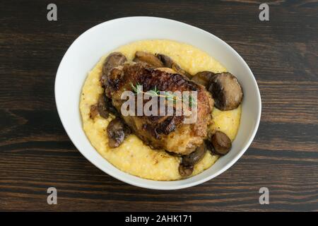 Geschmorte Hühnerkeule mit Pilzen und cremiger Polenta: cremiger Polenta überbacken mit in Scheiben geschnittenen Champignons und ein Geschmortes Hähnchen Schenkel Stockfoto