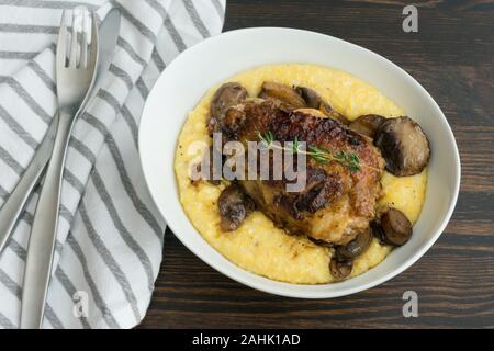 Geschmorte Hühnerkeule mit Pilzen und cremiger Polenta: cremiger Polenta überbacken mit in Scheiben geschnittenen Champignons und ein Geschmortes Hähnchen Schenkel Stockfoto