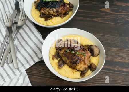 Geschmorte Hühnerkeule mit Pilzen und cremiger Polenta: cremiger Polenta überbacken mit in Scheiben geschnittenen Champignons und geschmorte Hühnerkeule Stockfoto