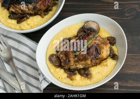 Geschmorte Hühnerkeule mit Pilzen und cremiger Polenta: cremiger Polenta überbacken mit in Scheiben geschnittenen Champignons und geschmorte Hühnerkeule Stockfoto