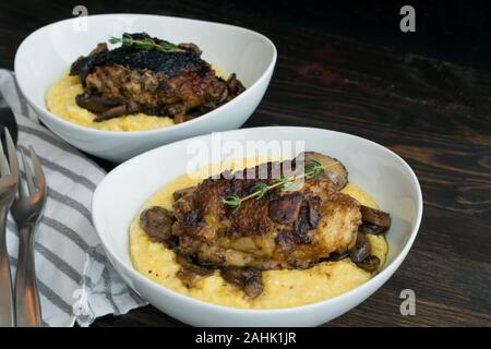 Geschmorte Hühnerkeule mit Pilzen und cremiger Polenta: cremiger Polenta überbacken mit in Scheiben geschnittenen Champignons und geschmorte Hühnerkeule Stockfoto