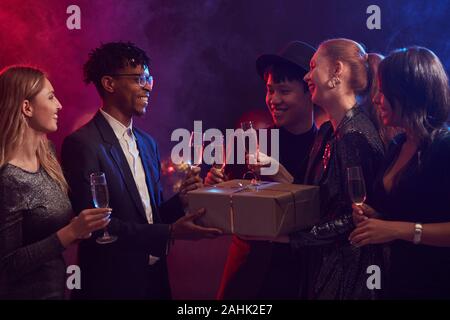 Multi-ethnischen Gruppe der elegante junge Menschen den Austausch von präsentiert während Partei in verrauchten Nachtclub Stockfoto