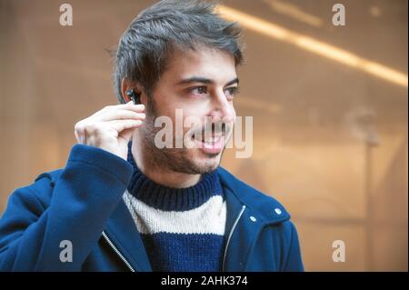 Hübscher junger Mann, setzen auf drahtlose Kopfhörer beim Gehen, Stadt Hintergrund. Stockfoto