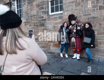Touristen fotografieren einer Piper Straßenmusik auf der Royal Mile, Edinburgh, Schottland. Stockfoto