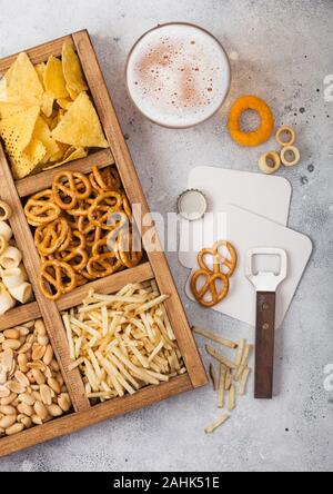 Glas Handwerk Lagerbier und Opener mit Box von Snacks auf leichte Küche Hintergrund. Brezel, salzig Kartoffelstifte, Erdnüsse, Zwiebelringen mit Nachos in Stockfoto