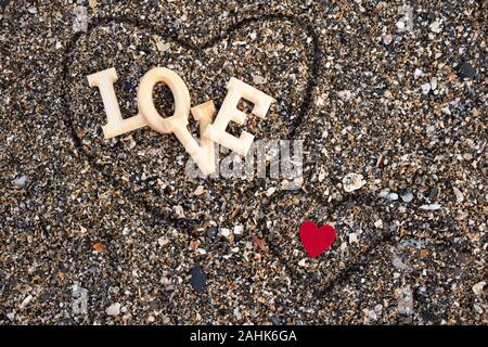 Holz- Buchstaben, die das Wort Liebe mit einem roten Herzen auf dem Hintergrund der Strand sand, innen ein Herz mit dem Finger gemacht. Konzept von San Valentine Stockfoto