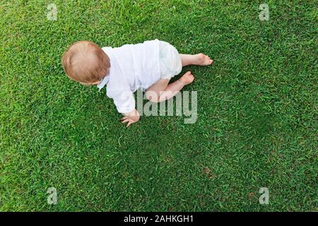 Wunderbares kleines Baby, das auf grünem Gras krabbelt Stockfoto