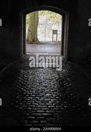 Licht auf nassem Kopfsteinpflaster Steine in einem dunklen feuchten Tunnel, der unter den erhaltenen alten Stadtmauer in der historischen baskischen Stadt Bayonne, Frankreich wider Stockfoto