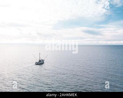 Ein kleiner alter Fischtrawler auf dem offenen Meer mit Wolken am Horizont. Stockfoto