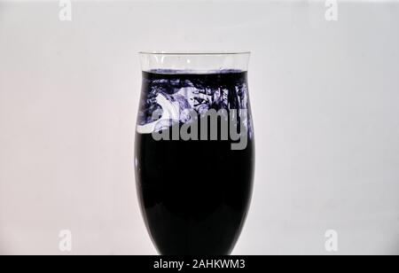 Blaue und schwarze Tinte fiel in einen Wein Glas Wasser auf einem weißen Hintergrund. Stockfoto