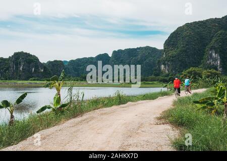 Touristen fahren Fahrräder durch die üppige Landschaft in Hoa Lư, Provinz Ninh Binh, Vietnam Stockfoto