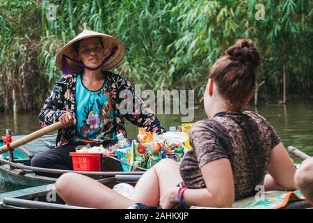 Eine Frau versucht, Süßigkeiten aus ihrem Boot zu einer touristischen auf ein anderes Boot in der Ngo Dong Fluss zu verkaufen, Provinz Ninh Binh, Vietnam Stockfoto