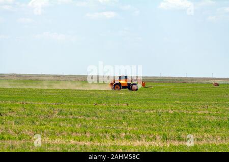 Einen landwirtschaftlichen Traktor Lader lasten Heuballen in einen Traktor Anhänger auf dem Feld Stockfoto
