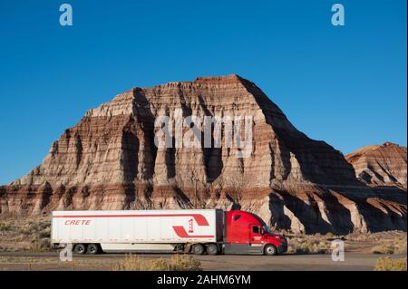Rote Lkw mit einem weißen Anhänger von Kreta fahren hinter einem Berg in Utah Stockfoto