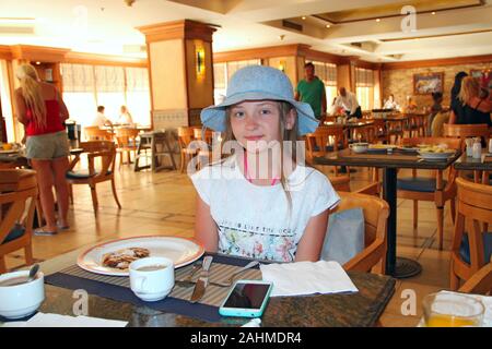 Moderne Kind lächelnd, während im Restaurant sitzen. Kleines Mädchen in hat ist ein Mittagessen im Restaurant. Mädchen in hat Posing beim Essen Stockfoto