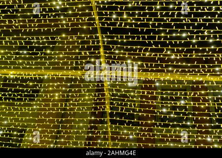 Eine festliche Girlande mit zahlreichen gelben Lichter am Kreuz Rahmen glänzt in der Dunkelheit vor dem Hintergrund der Gebäude. Bunten und magischen decorat Stockfoto
