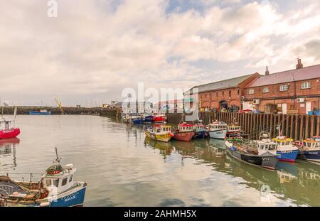 Der Hafen von Scarborough. Fischerboote im Hafen neben einem Wharf mit roten Backsteinbauten vertäut. Ein bewölkter Himmel über. Stockfoto