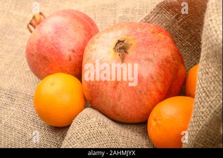 Zwei reife Granatäpfel und Mandarinen auf einem Hintergrund aus grobem Homespun Stoff close-up. Fitness Ernährung. Gesunde Ernährung Stockfoto