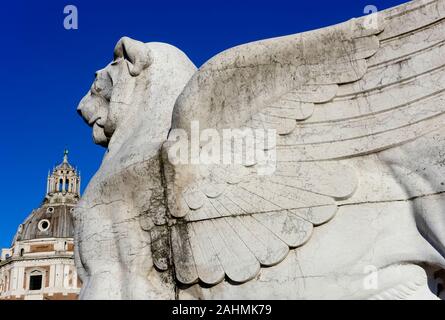 Geflügelte Löwe Statue, Denkmal für Victor Emmanuel II.. Altar des Vaterlandes. Im Hintergrund Kuppel der Kirche Heilige Maria von Loreto. Rom, EU. Nahaufnahme Stockfoto