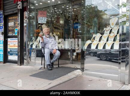 An einem warmen Tag, fallen einem Sikh Juwelier sitzt vor seinem Geschäft allein in seinen Gedanken. Auf 74th Street in Jackson Heights, Queens, New York City. Stockfoto