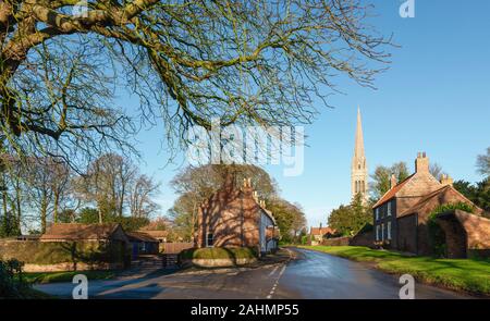 English Village Szene mit alten St Mary's Church durch Häuser und Bäume an einem schönen Tag im Winter im Süden von Dalton, Yorkshire, UK flankiert. Stockfoto