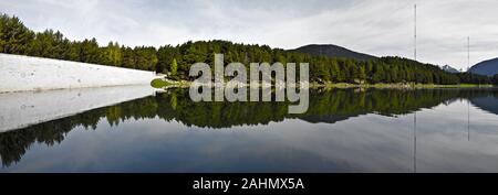 Das Panorama von Engolasters See in Andorra Pyrenäen. Der Damm ist auf der linken Seite, die Tanne Wald und den Himmel reflektieren in Wasser und fdie Blick auf Mou Stockfoto