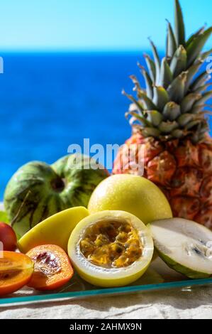 Tropische Früchte Sammlung, Custard Apple oder Grün reif cherymoia, Maracuja, Ananas, Mango, tamarillo Exotische Früchte auf blaues Meer Hintergrund in Stockfoto