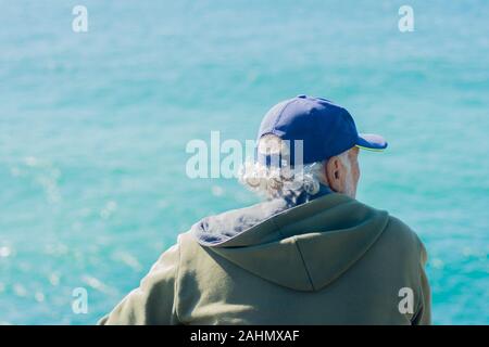 Rückseitige Ansicht des Herrn tragen Sweatshirt und Kappe auf dem blauen Meer. Das Konzept der Reflexion und gute Laune. Stockfoto