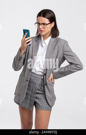 Junge verwirrte Student in Grau formale Abnutzung in Smartphone suchen Stockfoto