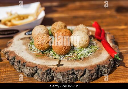 Käsebällchen und Kroketten auf einer Holzplatte closeup mit Kräutern und Pfeffer Stockfoto