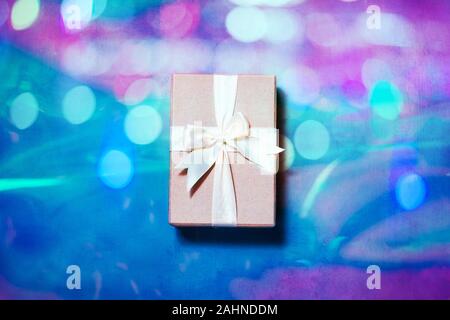 Geschenkbox mit Schleife über holografische Hintergrund. Minimale flach im Neonlicht Stockfoto