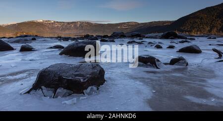Black Rock Felsbrocken drücken durch Thin Ice Shelf als Flut fällt in Norwegen Fjord. Stockfoto