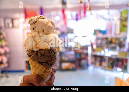 Eine Nahaufnahme und first person Perspektive der Mann hält eine Waffel Kegel mit zwei Kugeln Eis in einem Geschäft, mit einem bunten Store im Hintergrund Stockfoto