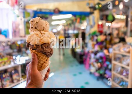 Eine Nahaufnahme und first person Perspektive der Mann hält eine Waffel Kegel mit zwei Kugeln Eis in einem Geschäft, mit einem bunten Store im Hintergrund Stockfoto
