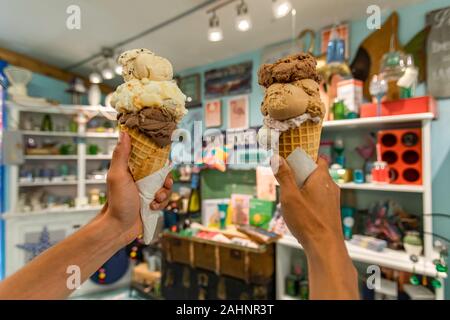 Eine Nahaufnahme und first person Perspektive eines Mannes zwei Waffeln Kegel mit holding Kugeln Eis in einem Geschäft, mit verschwommenen Geschenk Shop im Hintergrund Stockfoto
