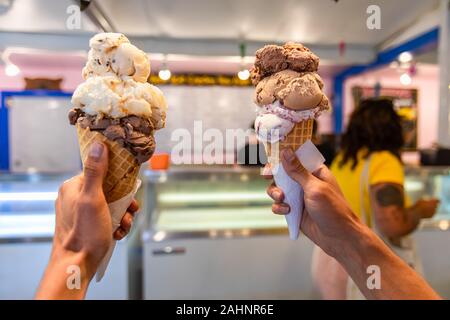 Eine Nahaufnahme und first person Perspektive eines Mannes zwei Waffeln Kegel mit holding Kugeln Eis in einem Geschäft, mit verschwommenen im Hintergrund Stockfoto