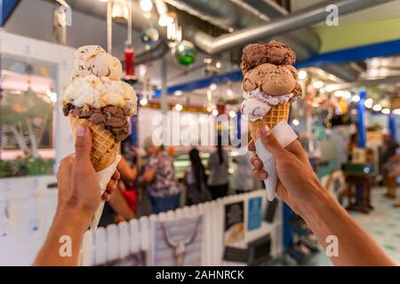Eine Nahaufnahme und first person Perspektive eines Mannes zwei Waffeln Kegel mit holding Kugeln Eis in einem Geschäft, mit verschwommenen Geschenk Shop im Hintergrund Stockfoto