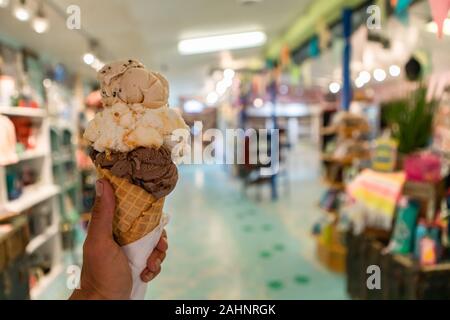 Eine Nahaufnahme und first person Perspektive der Mann hält eine Waffel Kegel mit zwei Kugeln Eis in einem Geschäft, mit einem bunten Store im Hintergrund Stockfoto