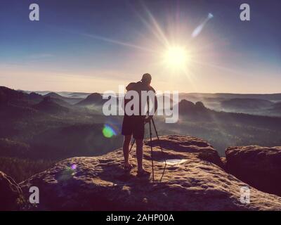 Mann, Fotograf, Foto auf Sonnenuntergang Berggipfel. Wanderer in Shorts und Rucksack auf verschwitzte Tasche Stockfoto