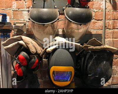 Sammlung von schweisser und Schleifer Sicherheit Helme / Gesichtsschutz, Handschuhe und staatsschützer Hängen an der Wand in einer Maschinenhalle Stockfoto