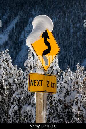 Eine Nahaufnahme von einem Schild, dass im Schnee bedeckt ist, ist die Straße wicklung für die nächsten zwei Kilometer. Stockfoto