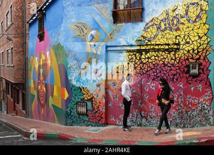 Paar auf Straße Ecke mit Wandmalereien und Graffiti an der Außenseite des Gebäudes in La Candelaria Stadtteil von Bogota, Kolumbien lackiert Stockfoto